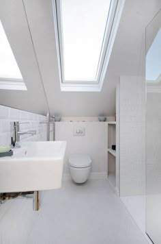 a white bathroom with a skylight above the toilet and sink in front of it