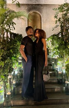 a man and woman standing next to each other in front of some potted plants