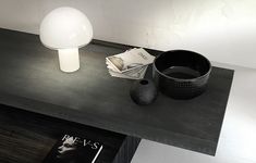 a table with a lamp, bowl and magazine on it next to a black vase