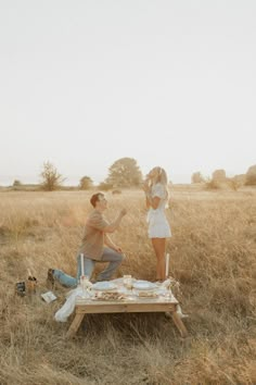 a man and woman sitting on top of a picnic table in the middle of a field