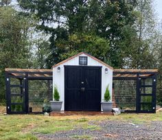 a black and white shed with potted plants on the roof is surrounded by trees