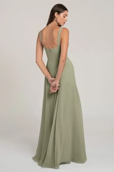 a woman in a long green dress with her back to the camera, looking down