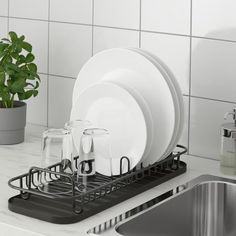 a dish rack with dishes in it next to a sink and a potted plant