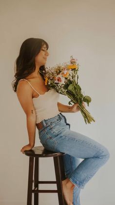 a woman sitting on top of a stool holding flowers