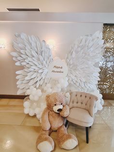 a teddy bear sitting on top of a chair in front of an angel wings backdrop