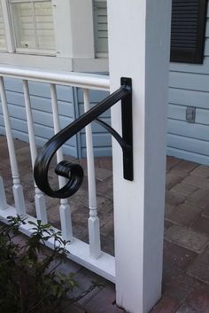 a black door handle on the side of a white porch railing with blue house in background