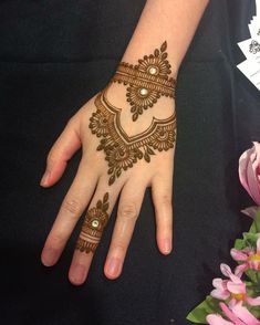 a woman's hand with henna on it and pink flowers in the background