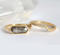 two gold rings with diamonds on them sitting in front of a crystal stone and glass container