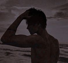 a man standing on top of a beach next to the ocean under a cloudy sky