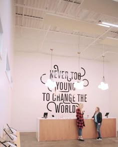 two women standing in front of a counter with a quote on the wall behind them