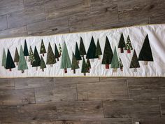 a quilted christmas tree wall hanging on a wood floor with white backing and green trees