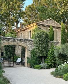 an old stone house surrounded by greenery and trees in the background is a gravel path leading up to it