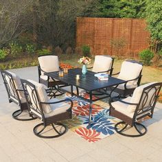 a patio table with chairs and a rug on the ground in front of a fence