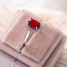 a ring with a large red stone surrounded by small white diamonds in a velvet box