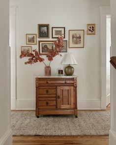 a wooden cabinet sitting in the middle of a room with pictures on the wall above it