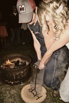 a woman bending over in front of an open fire pit with a hat on her head