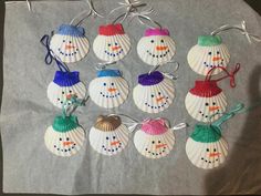 six seashell snowman ornaments are hanging on a piece of gray paper with string