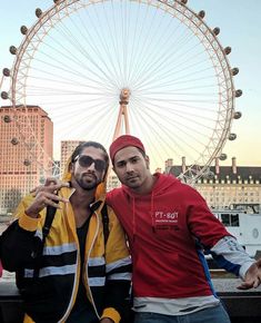 two men pose in front of a ferris wheel