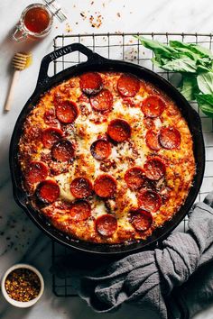 a pepperoni pizza in a cast iron skillet on a cooling rack next to other ingredients