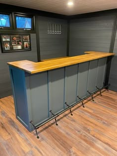 an empty bar in the middle of a room with wooden floors and gray walls, along with pictures on the wall