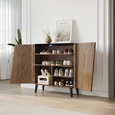 a wooden cabinet with shoes on it in a living room next to a potted plant