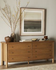 a wooden dresser with two vases on top of it and a painting above it