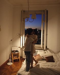 a man and woman standing on top of a bed in a bedroom next to a window