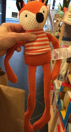 a hand is holding an orange knitted stuffed animal in front of a store display