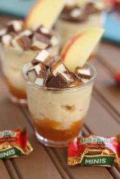 two glasses filled with dessert sitting on top of a wooden table next to an apple