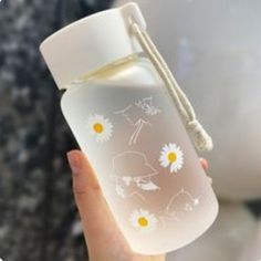 a hand holding a white glass bottle with flowers on it and a string attached to the top