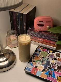 a table topped with books and a drink next to a lamp