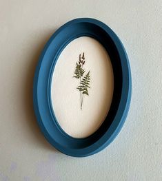 a blue frame with a pressed flower in it's center on a white wall