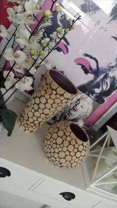 two vases sitting on top of a white table next to a painting and flowers