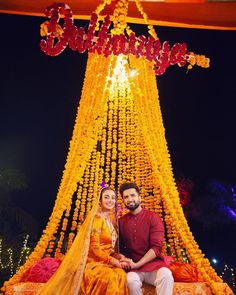 a man and woman sitting on a bed under a canopy covered in yellow garlands