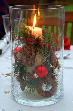 a candle that is sitting inside of a glass vase filled with pine cones and other decorations