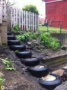 several tires are laying on the ground in front of a fence and some grass near a red brick building