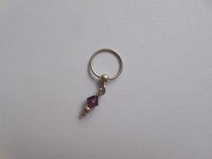 a silver ring with a small purple stone hanging from it's side on a white surface