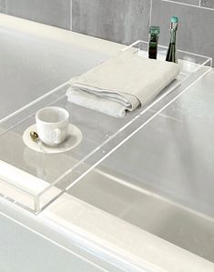 a white bath tub sitting next to a bathroom sink with a cup and saucer on it