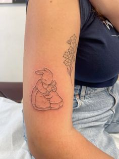 a woman with a tattoo on her arm holding a small bunny sitting in front of flowers