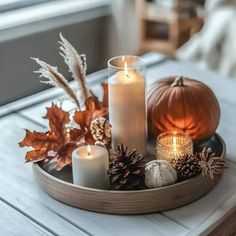 some candles are sitting on a tray with pumpkins and pineconis in it