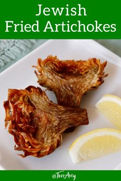 two pieces of fried artichokes on a white plate with lemon wedges