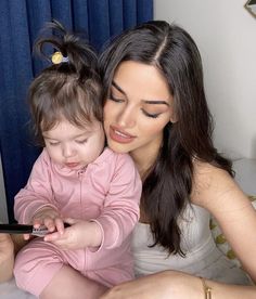 a woman holding a baby while looking at her cell phone with the child on her lap