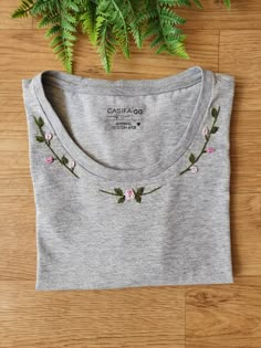 a grey t - shirt with pink flowers on the chest and green fern behind it