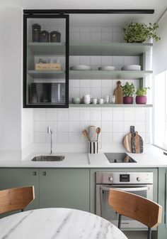 a kitchen with green cabinets and marble counter tops, white tile backsplash and open shelving