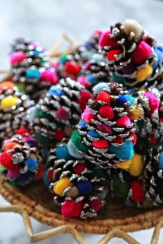 pine cones are decorated with colorful pom - poms on a wicker basket