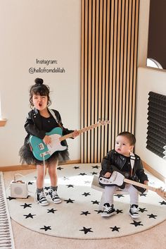 two small children are playing with guitars on the floor in front of a large wall