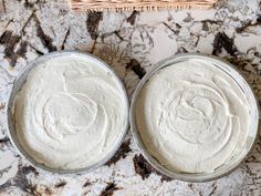 two tins filled with white frosting sitting on top of a marble counter next to a wicker basket