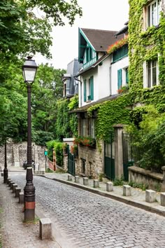 a cobblestone street lined with stone buildings and green shuttered windows on both sides