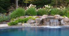 a pool with a waterfall in it surrounded by plants and flowers on either side of the pool