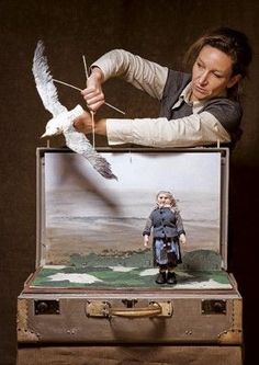 a man holding a bird over a doll in a suit case with an image of a seagull on it